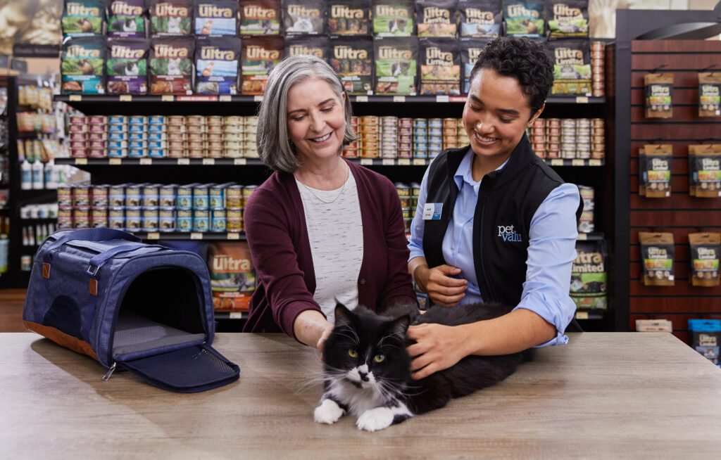 A Pet Valu franchisee smiles while helping a client and their pet cat.