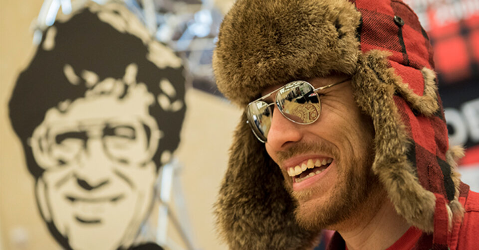 Ryan Smolkin appears wearing a trapper hat and aviator sunglasses. He's smiling.