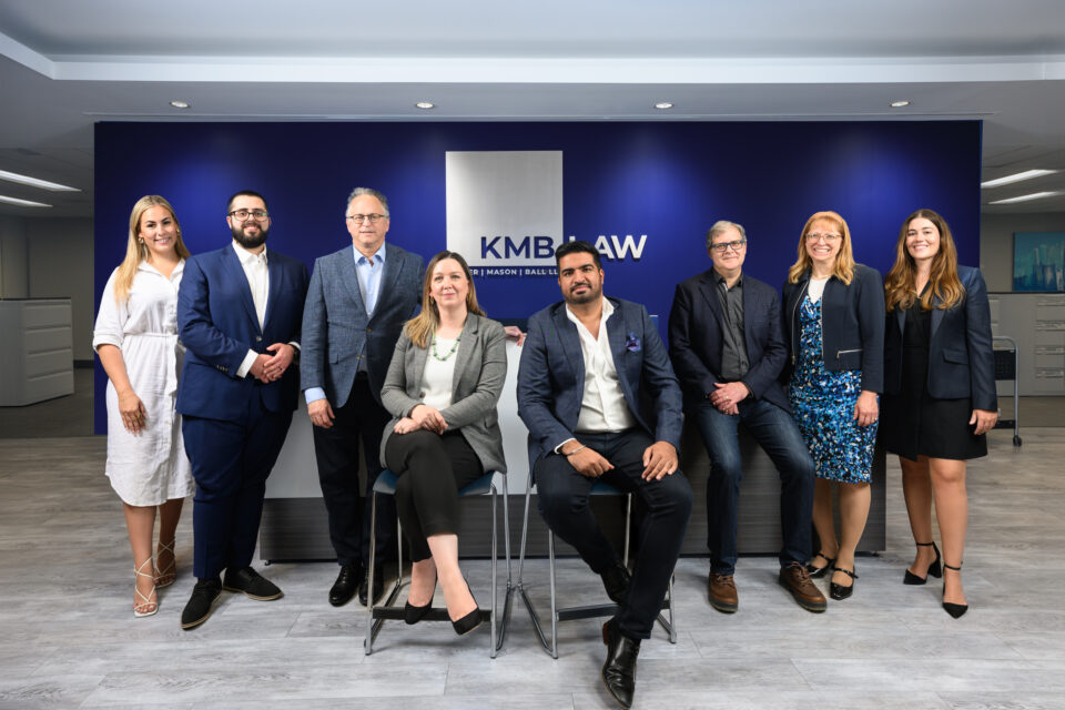 KMB Law and Hoffer Adler executives stand in front of a blue wall. The KMB Law logo