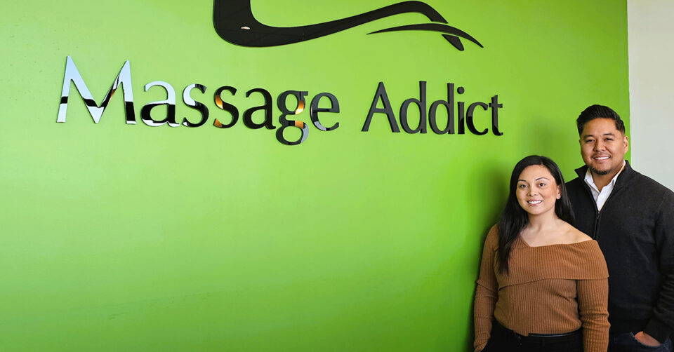 Christina and Justin Dabu next to Massage Addict sign on green wall